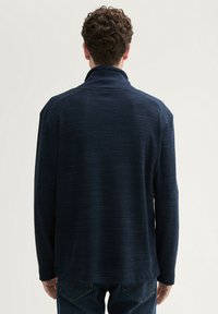 Marineblauer Pullover mit hohem Kragen und strukturiertem Stoff, ausgestattet mit langen Ärmeln und einem lässigen Schnitt, getragen mit blauen Jeans.