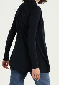 Langärmelige, dunkelmarine Cardigan mit lockerer Passform, strukturiertem Strickmaterial, abgerundetem Saum und seitlichen Schlitzen für zusätzlichen Bewegungsfreiraum.