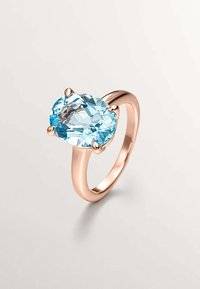 Anillo de oro rosa con una gran piedra preciosa ovalada de color azul claro, engastada en cuatro garras, y una banda lisa y pulida.