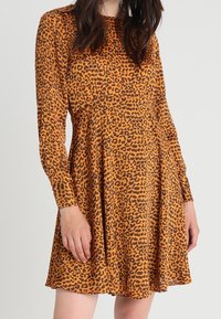 Leopardmönstrad klänning i orange och svart, lång ärm, utsvängd design, lätt tyg med en slät textur, plisserad midjedetalj.