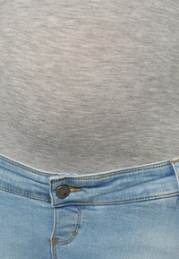 T-shirt de tecido texturizado em cinza, combinado com jeans de denim azul claro, apresentando fecho de botão e ligeira desfiagem na cintura.