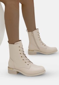 Botines beige de cordones, hechos de material sintético, con herrajes en tono dorado y cremallera lateral, que presentan un tacón de bloque texturizado.