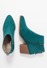 Paahdetyt nilkkurit meripihkanvihreällä mokkanahalla, joissa on palikkakorkoiset puiset korot, sivuvetoketjut ja terävät kärjet, näkyvissä ylä- ja sivukuvista valkoisella taustalla.