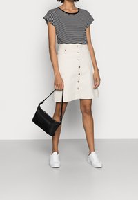 Top de manga corta a rayas negras y blancas, falda crema con botones en la parte delantera, bolso negro de hombro y zapatillas blancas sobre un fondo neutro.