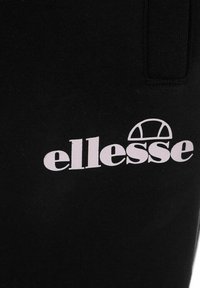 Tela negra con una textura acanalada que presenta un prominente logo blanco de "ellesse" y un elemento de diseño geométrico encima.