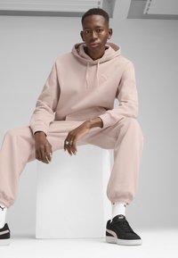 Lyserød hættetrøje med kængurulomme og snoretræk, parret med matchende joggers. Sorte sneakers med pink accenter og hvide sokker.