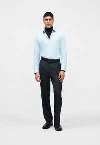 Camisa azul clara com colarinho, com um suéter preto de gola alta por baixo, combinada com calças cinza escuro riscas de giz e sapatos pretos.