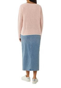 Pink knitted sweater with ribbed texture, layered over a light blue denim maxi skirt. Sneakers with metallic accents complete the outfit.