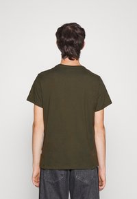 Oliven grøn bomulds-T-shirt med korte ærmer og rund hals, set fra ryggen. Har en afslappet pasform og glat tekstur.