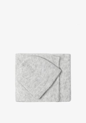 Un bonnet en laine tricoté gris clair et une écharpe assortie soigneusement pliés sur un fond blanc.