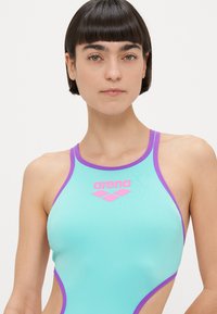 Aqua blå badedrakt med lilla detaljer og logo, med høy hals og utskjæringer på sidene, laget av glatt, elastisk materiale.