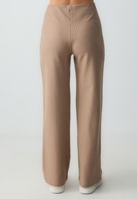 Tan gestreepte broek met een wijde pasvorm, een gladde textuur en een aansluitende taille. De zoom heeft een lichte flair naar de onderkant.