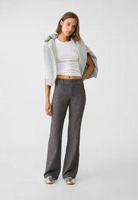 Pantalons gris à jambe large avec une texture subtile, assortis à un haut ajusté blanc et un sweat à capuche gris clair drapé sur les épaules. Chaussures argentées.