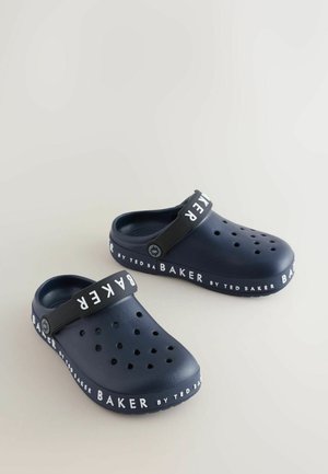 Zoccoli blu navy con un design solido, caratterizzati da una fascia con la scritta "TED BAKER" in bianco e fori di ventilazione sulla superficie superiore.