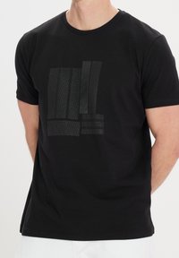Sort bomuld t-shirt med et geometrisk design i forskellige matte teksturer og linjer på forsiden. Rund hals, korte ærmer.