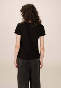 T-shirt in cotone nero con maniche corte, scollatura rotonda e vestibilità rilassata. Abbinato a pantaloni a gamba larga in denim scuro a vita alta.