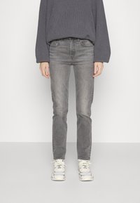 Jeans grigi con una vestibilità slim, lavaggio chiaro e un classico design a cinque tasche, abbinati a un maglione grigio in maglia e sneaker bianche.