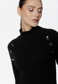 Czarny sweter z wysokim kołnierzem w prążki, z okrągłymi czarnymi guzikami na jednym ramieniu, charakteryzujący się dopasowanym krojem i miękką teksturą.