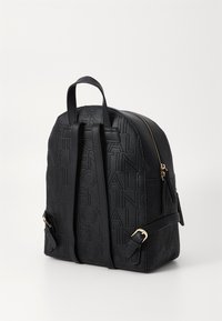 Crna ruksak s reljefnim uzorkom logotipa, zlatnim hardverom, podesivim trakama i odvojenim džepom sa zipom. Napravljen od teksturiranog materijala.