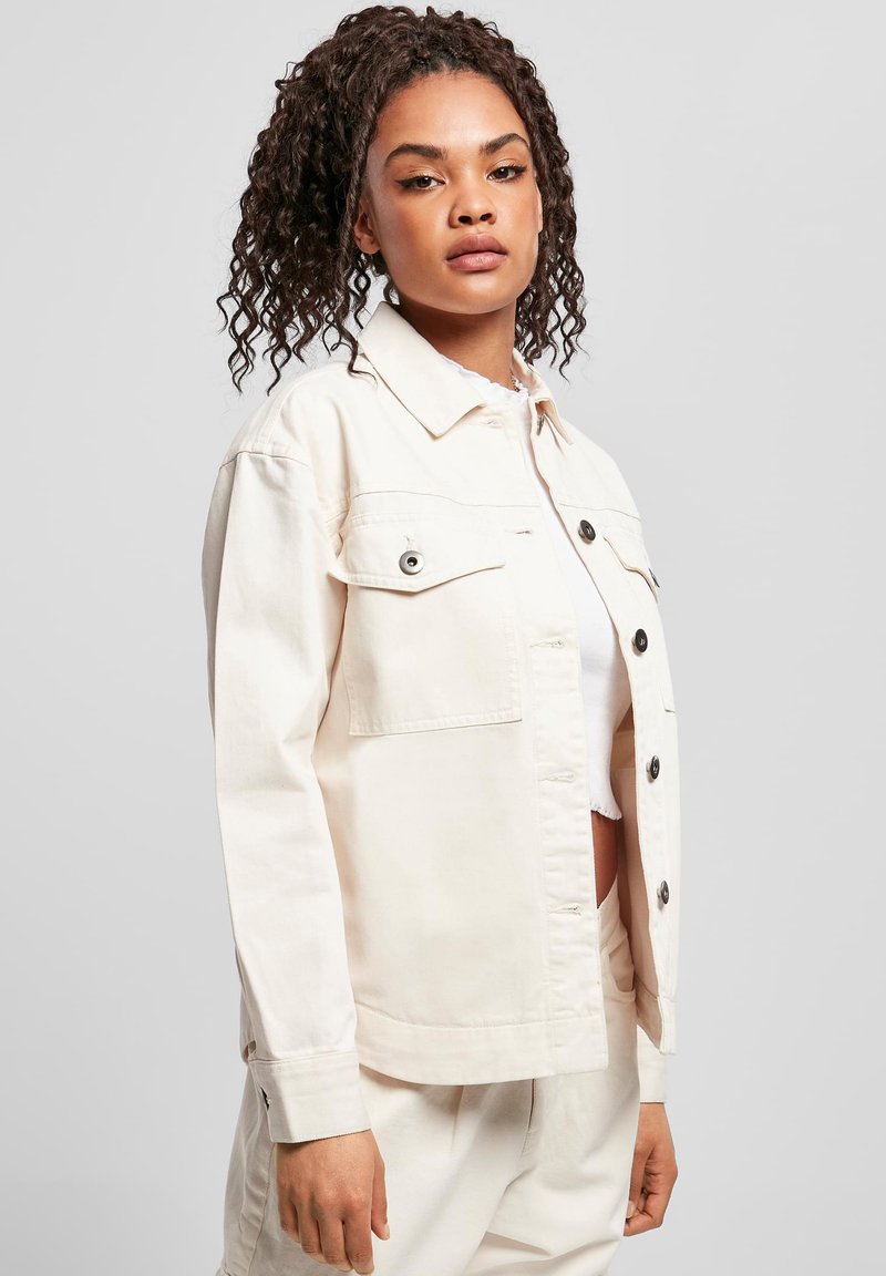 Lichtbeige denim jacket met twee borstzakken, zwarte knopen en een ontspannen pasvorm. Heeft een kraag en knoopsluitingen bij de mouwen.