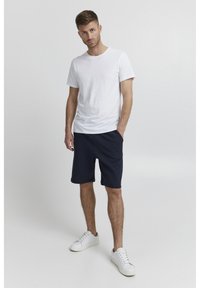T-shirt bianca in cotone a maniche corte abbinata a pantaloni corti blu navy, con vita elastica. Completata con sneakers bianche.
