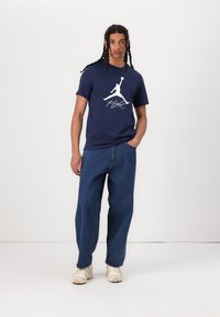 Marineblå bomulds t-shirt med et hvidt logo og teksten "Flight." Sat sammen med løstsiddende blå denim jeans og sneakers i cremefarve.
