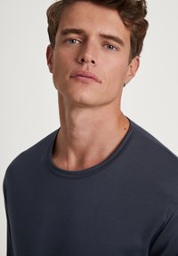 Chemise à manches longues gris foncé avec col rond, texture lisse et coutures minimales, présentant un design ajusté et un tissu doux.