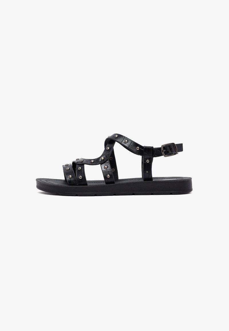 Black sandal featuring multiple straps adorned with metallic studs, a flat sole, and an adjustable buckle for fit.