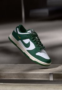 Baskets Nike Dunk vert et blanc en matériaux suède et cuir, avec un Swoosh vert et des accents jaunes, et une semelle en caoutchouc.