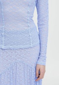 Abito in pizzo lavanda chiaro con maniche lunghe, caratterizzato da motivi floreali, superficie strutturata e dettagli arricciati all'orlo.