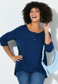 Marineblauw langarmshirt met een ronde hals, drie knopen en een losse pasvorm, gecombineerd met een lichtblauwe handtas met een geplooide band.