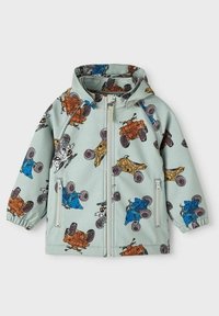 Veste légère verte avec fermeture éclair sur le devant, poignets élastiques et un motif répétitif de véhicules tout-terrain colorés.