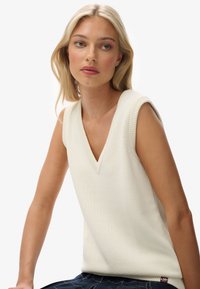 Witte mouwloze V-hals gebreide top met ribbelafwerking en een ontspannen pasvorm, gecombineerd met een gestreepte blauwe onderkant.
