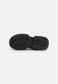 Black rubber shoe sole with a segmented tread pattern, featuring deep grooves for traction and a smooth central section.
