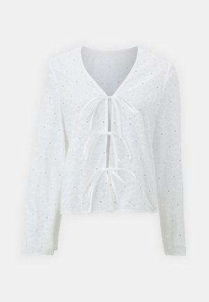 Cămașă albă cu mâneci lungi și decolteu în V, având trei legături în față și un model floral cu perforații. Material ușor, cu o textură distinctă.