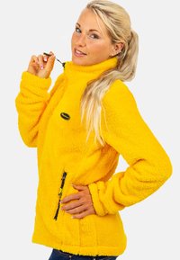 Gele fleece jas met een hoge kraag, ritsdetails op de zijzakken en een gestructureerde, pluizige uitstraling voor warmte.