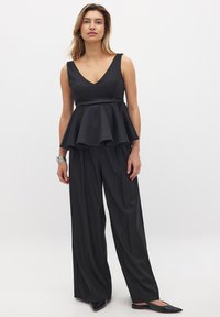 Top peplum nero con scollo a V e corpino aderente, abbinato a pantaloni larghi a gamba ampia, entrambi in un tessuto liscio e tessuto.
