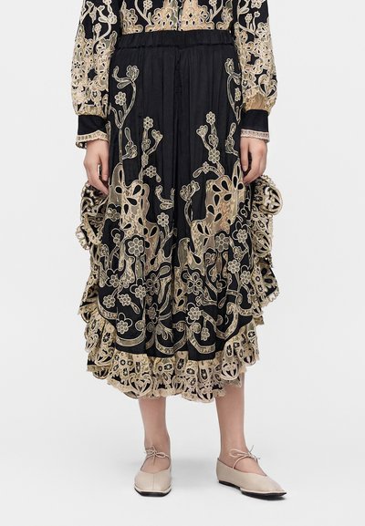 Jupe midi noire avec broderie florale beige et bordure en dentelle, portée avec des ballerines pointues beige.