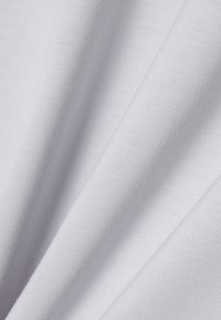 Tissu blanc doux avec une texture fine tricotée, présenté en plis délicats montrant une surface lisse et un ombrage subtil.