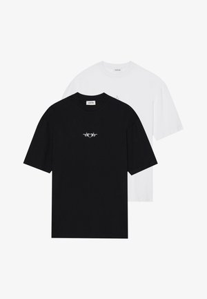 Pár krátkych rukávov tričiek z čierneho a bieleho bavlneného materiálu. Na čiernom tričku má malé biele tribal srdce.