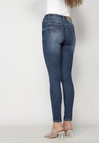 Smala jeans i mörkblå denim, med en mid-rise midja, bakfickor med dekorativ sömnad och ankellång passform.