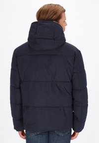 Marineblå pufferjakke med hætte, der har et quiltet design, tyk polstring og lange ærmer. Bagvægten viser en glat tekstur og enkelt styling.