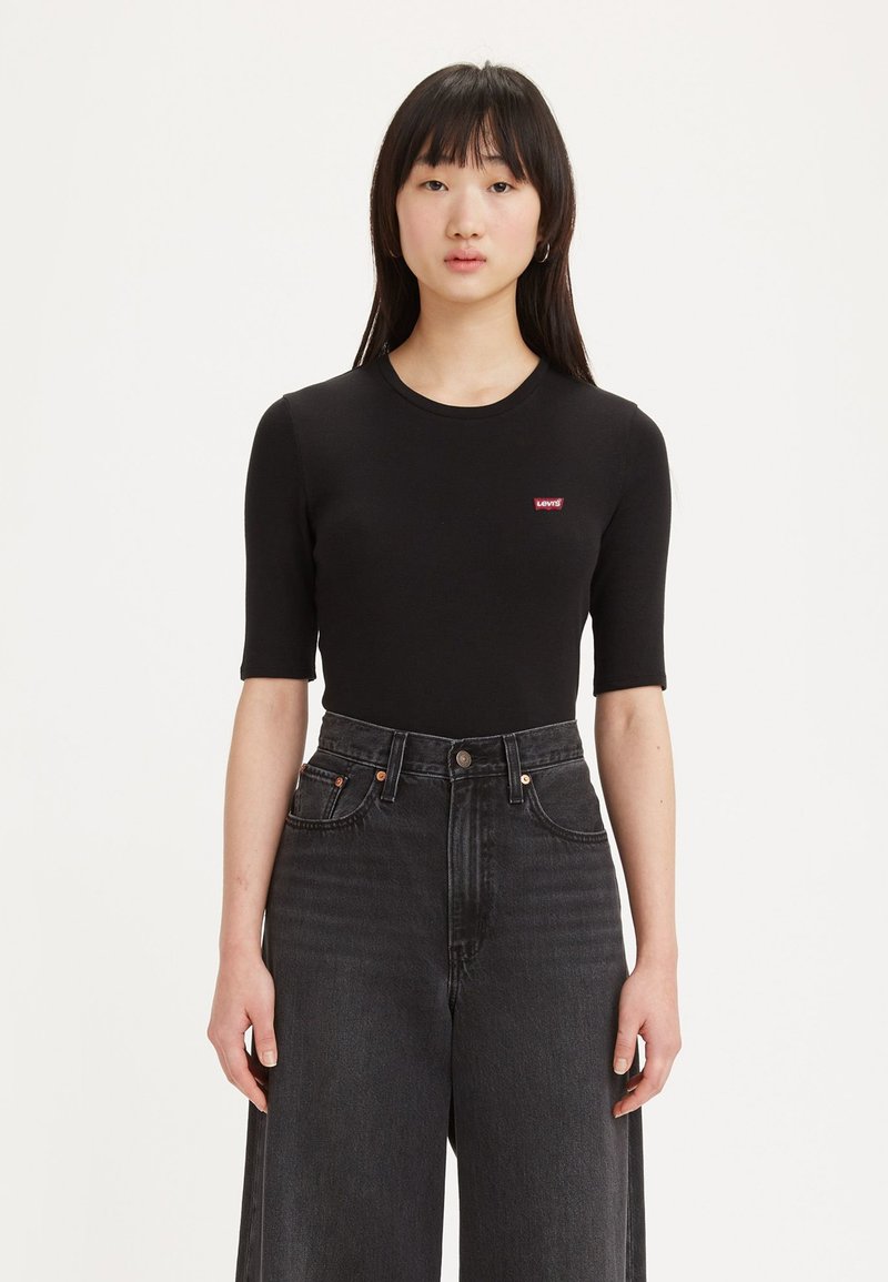 Haut noir à manches courtes avec col rond et patch logo rouge Levi's, associé à un jean en denim noir taille haute et jambes larges.
