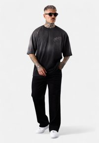 Oversized black T-shirt with a faded finish and pink lettering, paired with black trousers and white sneakers. Sunglasses complete the look.