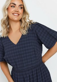 Tummansininen mekko, jossa on V-pääntie, lyhyet hulmuavat hihat ja teksturoitu ruutukuosi sekä joustava vyötärö.