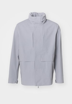 Ljusgrå jacka med hög krage, knappstängning och en kort design. Har en mjuk textur med minimalistisk stil och inga synliga mönster.