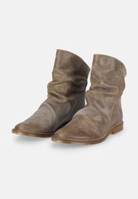 Botas de cuero marrón hasta el tobillo con un diseño holgado, superficie texturizada, punta afilada y suela de goma plana. Estilo minimalista sin herrajes.