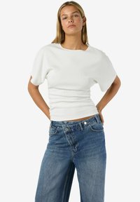 Balts ribots īsroku tops ar brīvu piegriezumu. Kopā ar augsta vidukļa ziliem platajiem džinsiem ar pogu aizdari un klasisko šuvi.