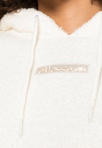 Witte fleece hoodie met textuurstof, voorzien van een geborduurd logo in beige, verstelbare trekkoorden en een V-vormige halslijn.