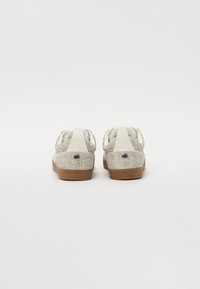 Hvite sneakers med en glitrende sølvnetting overdel, tan gummisåle og en glatt hvit hælakkent. Har to løkkede drailer.